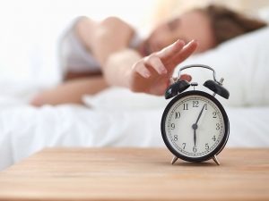 Young sleeping woman and alarm clock in bedroom at home .